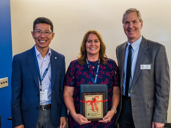 three people standing, person in center holding award