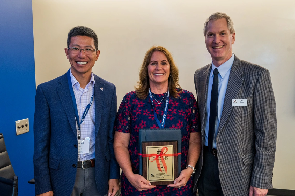 three people standing, person in center holding award
