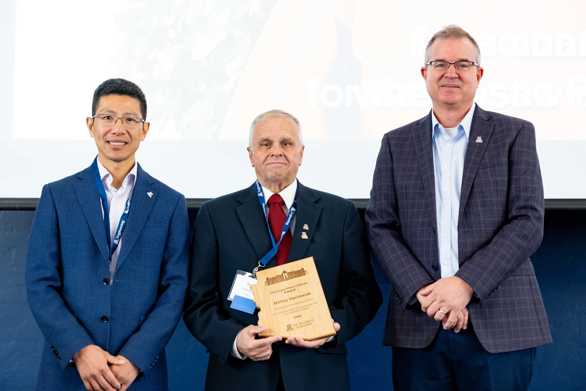 three people standing, person in middle holding an award