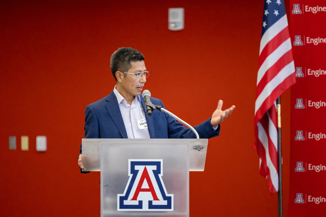 A man in a blue suits peaks on a glass podium.